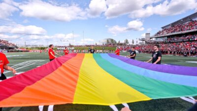 fans holding a rainbow Pride flag on the field at TD Place