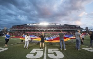 fans holding a pride flag on the field during the national anthem