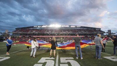 fans holding a pride flag on the field during the national anthem