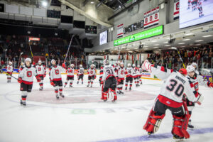 67's players celebrating on the ice after the game raising their sticks to the crowd