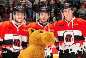 Image of 3 67's players posing in the Teddy Bear Toss jerseys