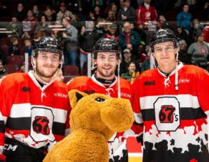 Image of 3 67's players posing in the Teddy Bear Toss jerseys